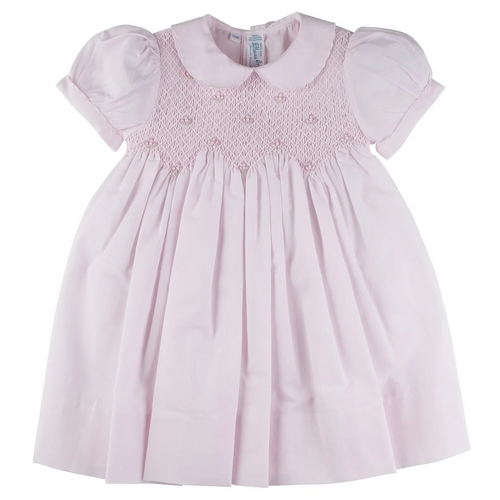 An utterly precious little girl's dress from Feltman Brothers! Scalloped stitching lines both the collar and puffed sleeves of this sweet looking dress, making it a perfect choice for your little darling. The smocking is covered in a beautiful diamond stitching and is embellished with hand embroidered clover flowers with a delicate pearl in the center of each. A zigzag design ends off the smocked bodice, and then continues into classy pleats down the length of the dress. Ties in the back with a lovely bow f